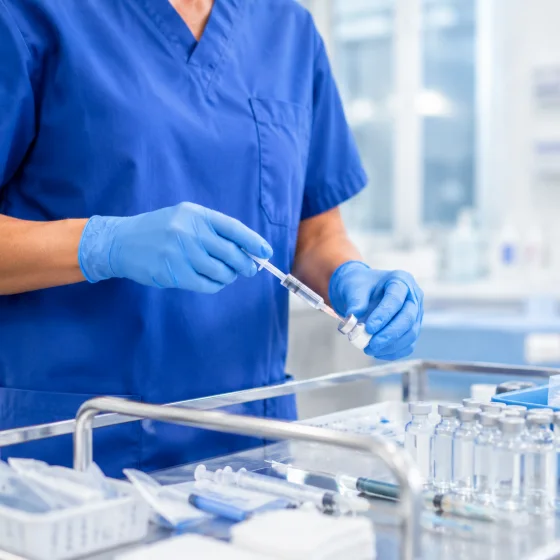 A nurse in gloves preparing a syringe at a clinical supply trolley